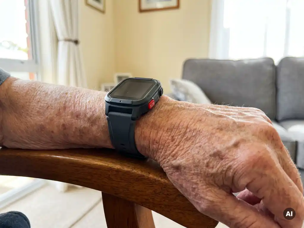 Smartwatch met SOS-knop om de pols van een oudere persoon, rustend op een houten armleuning in een lichte woonkamer.